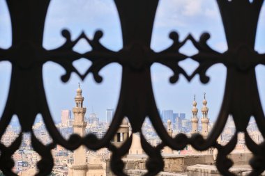 Kahire silueti karmaşık geleneksel İslami mashrabiya kafes işçiliğiyle ele geçirildi. Ön planda çok sayıda Sultan Hasan camii minaresi ve yüksek binalar dekoratif demir desen yer alıyor.
