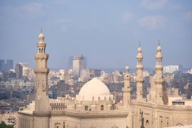 Sultan Hasan camii, modern şehir siluetinin arka planına karşı kurulmuş. Geleneksel İslami mimari ile Mısır 'ın Kahire kentsel binaları arasındaki zıtlık
