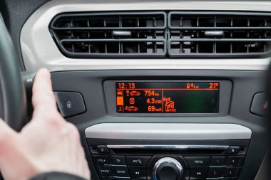 Arabanın ön panelinde çeşitli dijital göstergeler görülebilir. Sürücünün eli direksiyonu tutar.