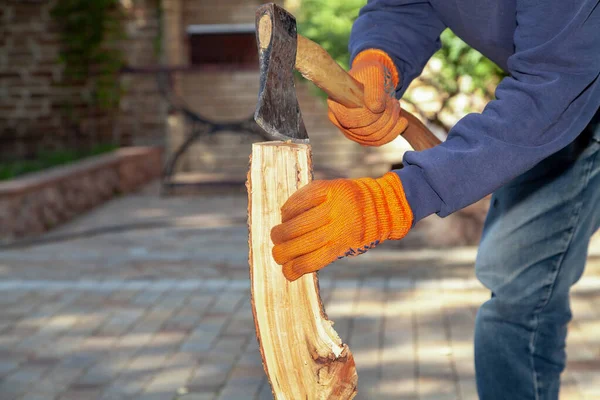 We prepare firewood for the barbecue. Hands in orange gloves chop a log on a stump with an ax on a sunny da