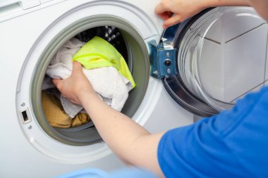 Hands putting dirty laundry in a front-loading washing machin