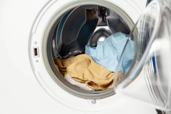 A pile of dirty laundry lies inside a modern front-loading washing machine. Close-u