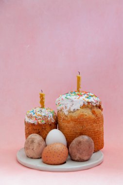 Paskalya 'da hayat. İki paskalya pastası ve yumurtalar pembe arka planda yuvarlak bir stantta duruyor. Mumlar Paskalya pastasına konur
