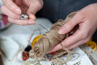 İğneci kadının elleri iğneyi orta parmağındaki yüksük yardımıyla halat bobinine batırır. Kapat.