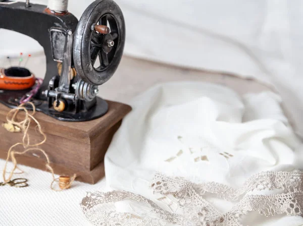 A vintage manual sewing machine stands on a white cloth. On it is a decorative ceramic pincushion in the form of a Dutch shoe
