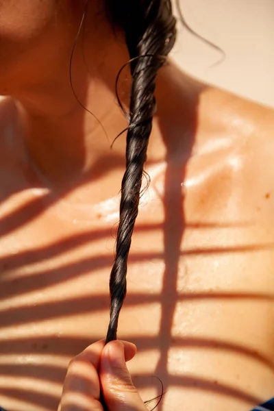 濡れた黒い髪のピグテールを閉じます 女性の日焼けした裸の肩の後ろ ヤシの木の枝の胸の影に — ストック写真