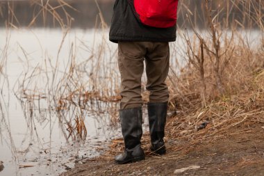 Siyah lastik çizmeli bacaklar nehrin kıyısındaki kıyıda duruyor.
