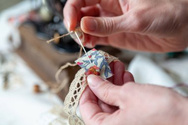 Bir iğnecinin elleri dantel bir kurdeleye iğneyle küçük bir kumaş parçası diker. Kapat.