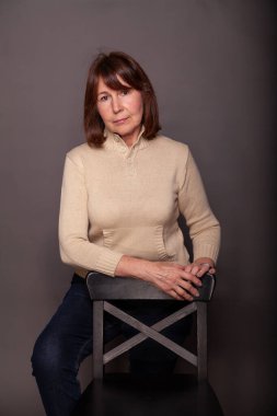 Karanlık bir monofonik arka plana dokunmadan bir kadının portresi. Bej kazaklı yaşlı güzel kadın çerçeveye bakıyor.