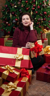 Yeni yıl hayalleri gerçek oluyor. Güzel genç bir kadın Noel hediyeleriyle dolu kutularla çevrili oturuyor. Arka taraftaki dekore edilmiş Noel ağacı