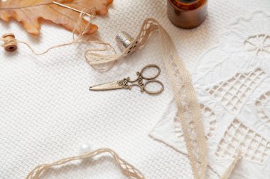 Hayat dikiyorum. Sarı renkli pirinç makas ve açılış örgüsü beyaz bir kumaşın üzerinde. Yukarıdan bak. Dantelin yanında. Tepesinde bir yüksük ve bir meşe ağacı uzanır.