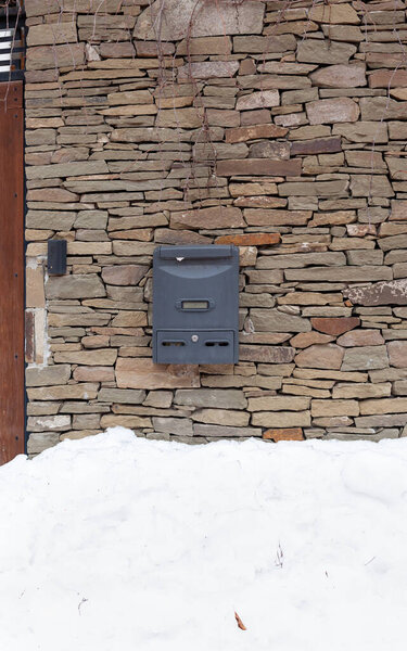 почтовый ящик весит на каменном заборе. Под ним высокий снежный ком.