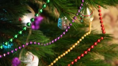 Çeşitli oyuncaklar ve yuvarlak boncuklardan oluşan uzun çelenkler Noel ağacının yeşil dallarında asılı. Yakın plan.
