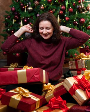 Noel hediyeleri aldım. Mutlu genç bir kadın, bir Noel turnesinin arka planında hediye kutularının içinde oturuyor.