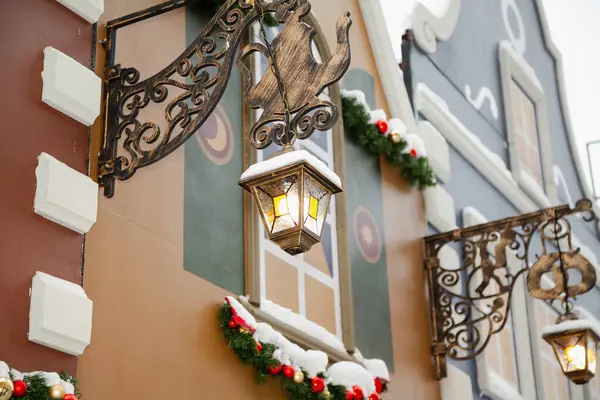 A fake wall of a building at a Christmas market. Street decorations in the style of small English houses. Panel bracket cantilever side sign in the form of a metal teapot and antique lanter