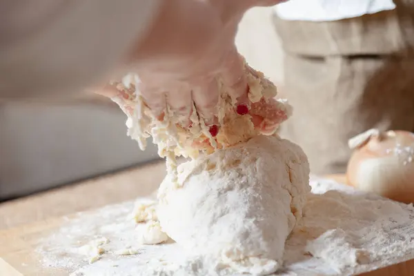 stock image A piece of dough in flour lies on a board and women hands above i