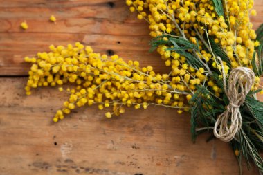 Bahar etüdü. Sarı mimozanın bir dalı tahta tahtalarda yatar. Üstte numara şeklinde bir ip var. 