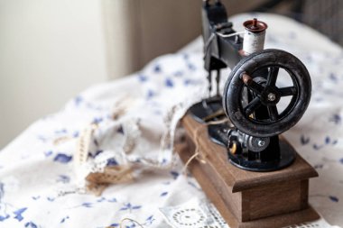 Klasik bir el yapımı dikiş makinesi mavi desenli beyaz bir kumaşın üzerinde duruyor. Üstteki beyaz eşik makarası
