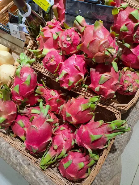 Many dragon fruits lie in wicker baskets on sale in a supermarket. Pitahaya or pitaya is the common name for the fruits of several species of cacti from the genera Hylocereus and Stenocereus