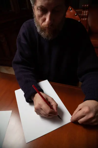 A man with a beard writes a letter with an old wooden pen with a metal pen. Nearby is an inkwel