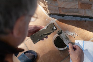 Evin duvarına fayansları monte ediyoruz. Bir el, dar bir mala kullanarak düz doğal taş fayanslara özel bir yapıştırıcı katmanı uygular. Kapat.