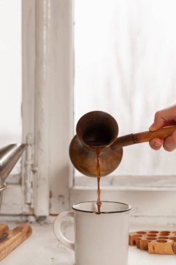 Pirinç hindiden gelen kahveyi beyaz bardağa doldurdum. Kupa geniş beyaz bir pencerenin üzerinde duruyor.