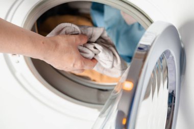 Hands putting dirty laundry in a front-loading washing machine. Close-u