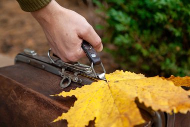 Bir adamın elinde bir seyahat çantası ve bir akçaağaç. Büyük sarı bir akçaağaç yaprağı deri bir çantada yatıyor.