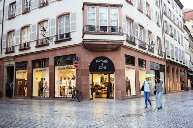 Strasbourg, Fransa - 10 Eylül 2022: Strasbourg 'un merkezindeki Baba ve Oğulları moda mağazasının önünde şemsiyeli genç kızlar yürüyor