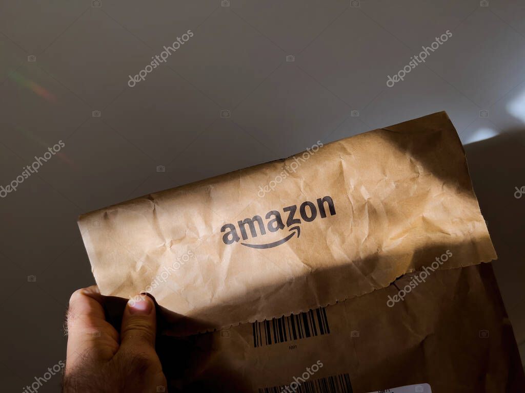 Paris, France - Oct 4, 2022: POV male hand holding Amazon prime cardboard parcel paper recycled bag - white abstract background