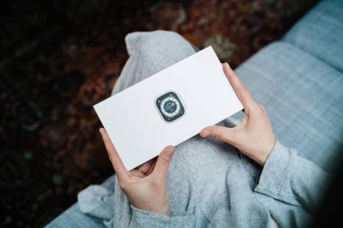 Londra, Birleşik Krallık - Bölüm 28, 2022: POV 'lu kadın dayanıklılık sporu gibi uç aktiviteler için tasarlanmış yeni Apple Watch Serisi Ultra' yı gösteren paketi elinde tutuyor - oturma odası koltuğu -