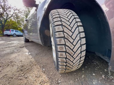 Close-up macro shot of a winter tire covered with dust - brand new wheels for the upcoming cold season - mandatory protection during cold weather - SUV in background