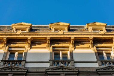 Low angle view close-up shot of the upper part of an elegant stone and white Haussmann building with balconies and blue sky in Paris