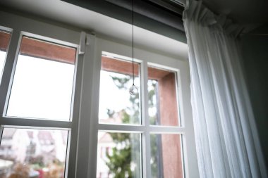 Low angle view of crystal rainbow maker suncatcher hanging near the window on a rainy day