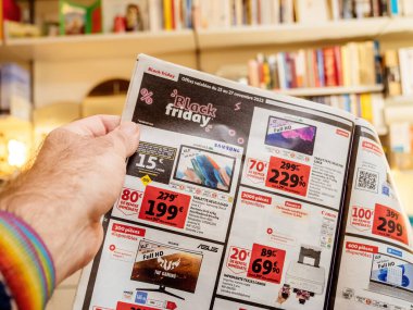 Paris, France - Dec 2, 2022: Man reading Auchan France leaflets supermarket chain selling furniture, electronics home object special black friday prices with Vitsoe 606 shelves in background