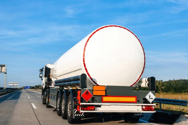 Rear view of a big fuel tanker truck driving on empty highway shipping fuel gas - clear blue sky in fast delivery cargo shipping of environmentally products..