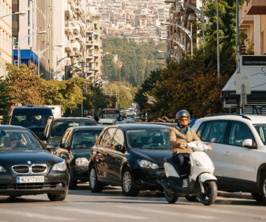 Thessaloniki, Greece - Oct 30, 2014: Defocused view of cars motorcycles mopeds waiting at red light with Thessalonique cityscape apartment buildings on a hill in background - square image