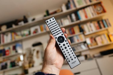 Frankfurt, Germany - Feb 23, 2023: POV male hand holding new Onkyo RC-816C remonte control with USB NET, CD, Phono and other buttons in living room with Vitsoe shelves in background
