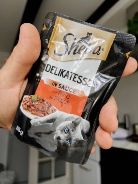 Paris, France - Sep 13, 2022: POV male hand holding pouch with Sheba wet cat food Jelly with taste - modern kitchen background preparing to feed the pet cat animal