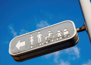 Beyaz metinlerle dolu göz kamaştırıcı mavi bir gökyüzü. Görünüşte her kelime halka açık bir tuvalet için hafif bir meltem işaretiyle uçuyor.