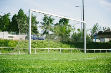 Güneş ışığı bir futbol sahasındaki yemyeşil çimleri aydınlatır ve arka planda çözülmüş bir kapı vardır. Başarının ve takım ruhunun mükemmel bir temsili.