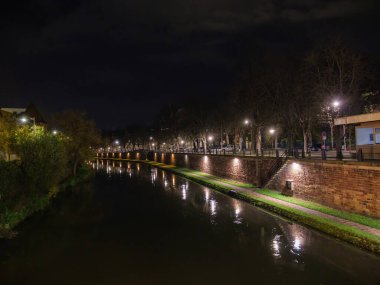 Alsace, Strasbourg 'daki pitoresk bir akşam sahnesi, şehrin ışıklarıyla aydınlatılan, Ill Nehri' ni ve inşa edilmiş yapı ve ağaçlarla kaplı kanal su yolunu yansıtan.