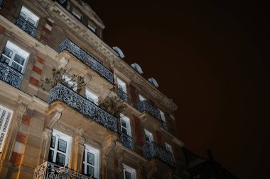 Birçok penceresiyle aydınlatılmış görkemli bir bina gece gökyüzüne karşı duruyor. Heybetli Hausmanya mimarisi şehrin ihtişamının bir göstergesidir.