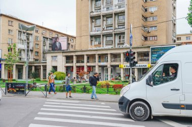 Bükreş, Romanya - 1 Ekim 2015: Her türlü insan ve araçla dolu hareketli bir şehir caddesi. Arabalar, kamyonlar ve diğer ulaşım araçları geçerken yayalar yüksek bir binanın önünden geçiyorlar.