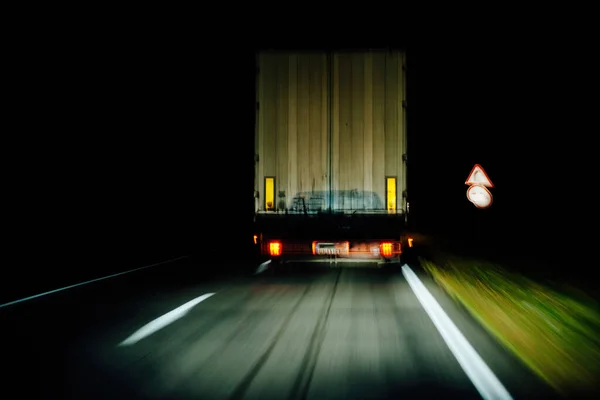 暗闇の中で運転する貨物トラックは 反射と光の跡を残して その目的地に向かうときに明るい光によって照らされます — ストック写真