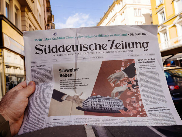 Paris, France - Mar 20, 2023: Suddeutsche Zeitung breaking news of UBS historic acquisition of rival Credit Suisse Group AG - male hand buying press at press kiosk - city background