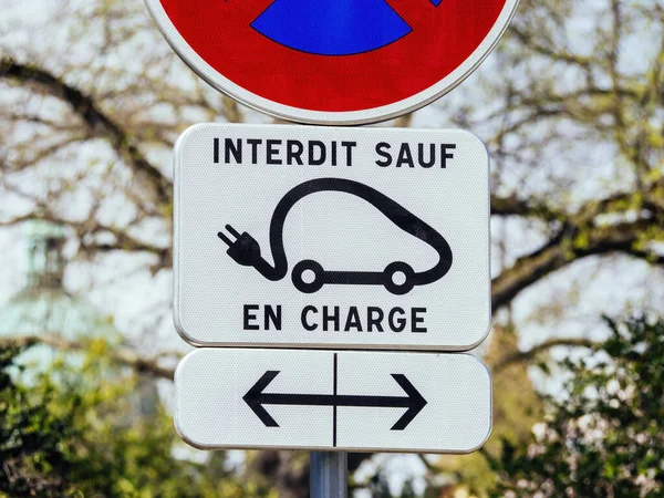 A street sign illuminated by the sunlight, guiding cars along a road - with symbols and text in western script. text in french language translated except electric vehicles -interdit sauf electric
