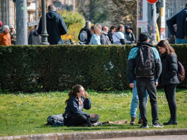 Strasborg, Fransa - 29 Mart 2023: Fransa 'nın Strazburg kentindeki Republique Park' ta güneşli bir günün tadını çıkaran bir grup yetişkin. Yeşillik ve güzel mimari cennet gibi doğal bir ortam yaratır.