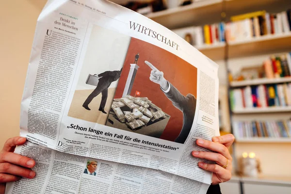 フランス 2023年3月21日 女性がリビングルームの中にドイツの新聞を持ち スイス銀行の信用スイスのスキャンダルについて読み このマスメディアでより多くの情報を探しています — ストック写真