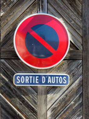 Antika bir kırmızı tabela modern bir şehir garajından çıkan arabaları uyarır, Fransız şehir girişi ışıkla aydınlatılır ve ahşap kapıyla çevrilidir.